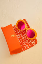 Barbie Sol Kyst round orange sunglasses with pink reflective lenses on an open matching case.