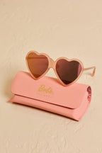 Barbie x Sol Kyst heart-shaped sunglasses displayed with a pink branded case on a textured surface.