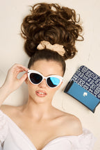 Model wearing women's Barbie cat eye sunglasses next to blue patterned case - top view.