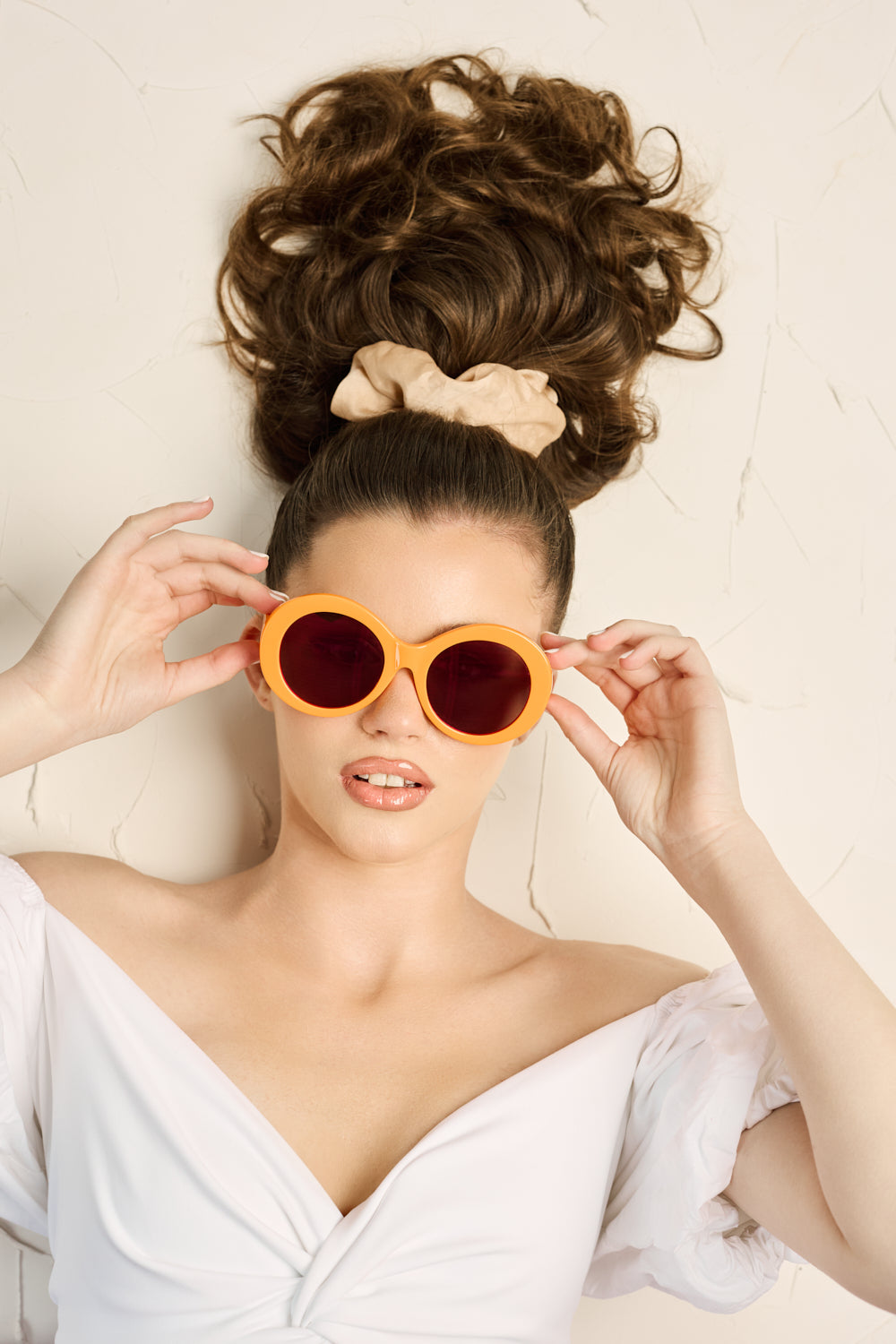 Women in front of beige background wearing Sol Kyst Barbie sunglasses with orange frames and tinted lenses in a white dress.