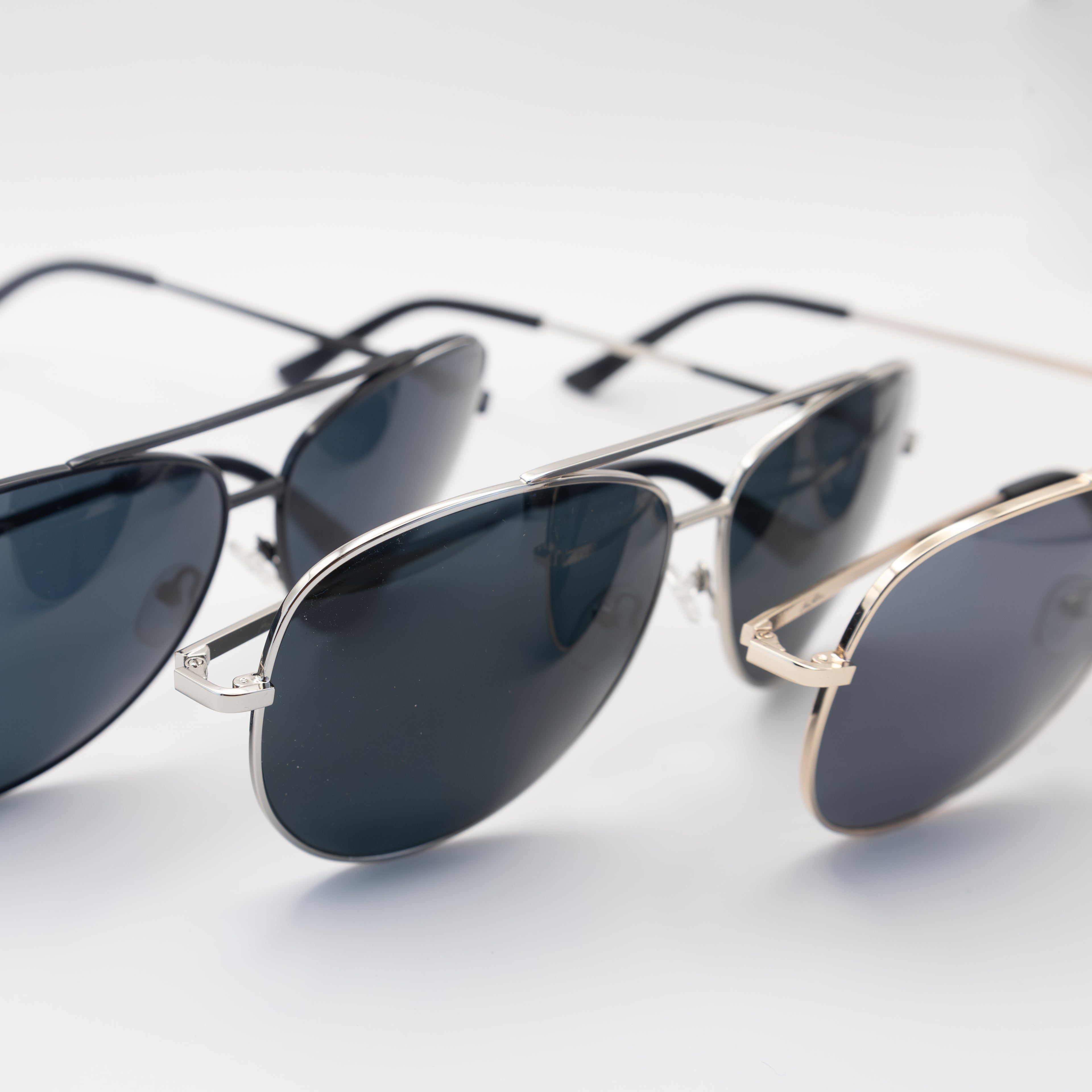 Close-up of three Sol Kyst women's aviator sunglasses in black, silver, and gold frames with dark polarized lenses, arranged on a white surface.