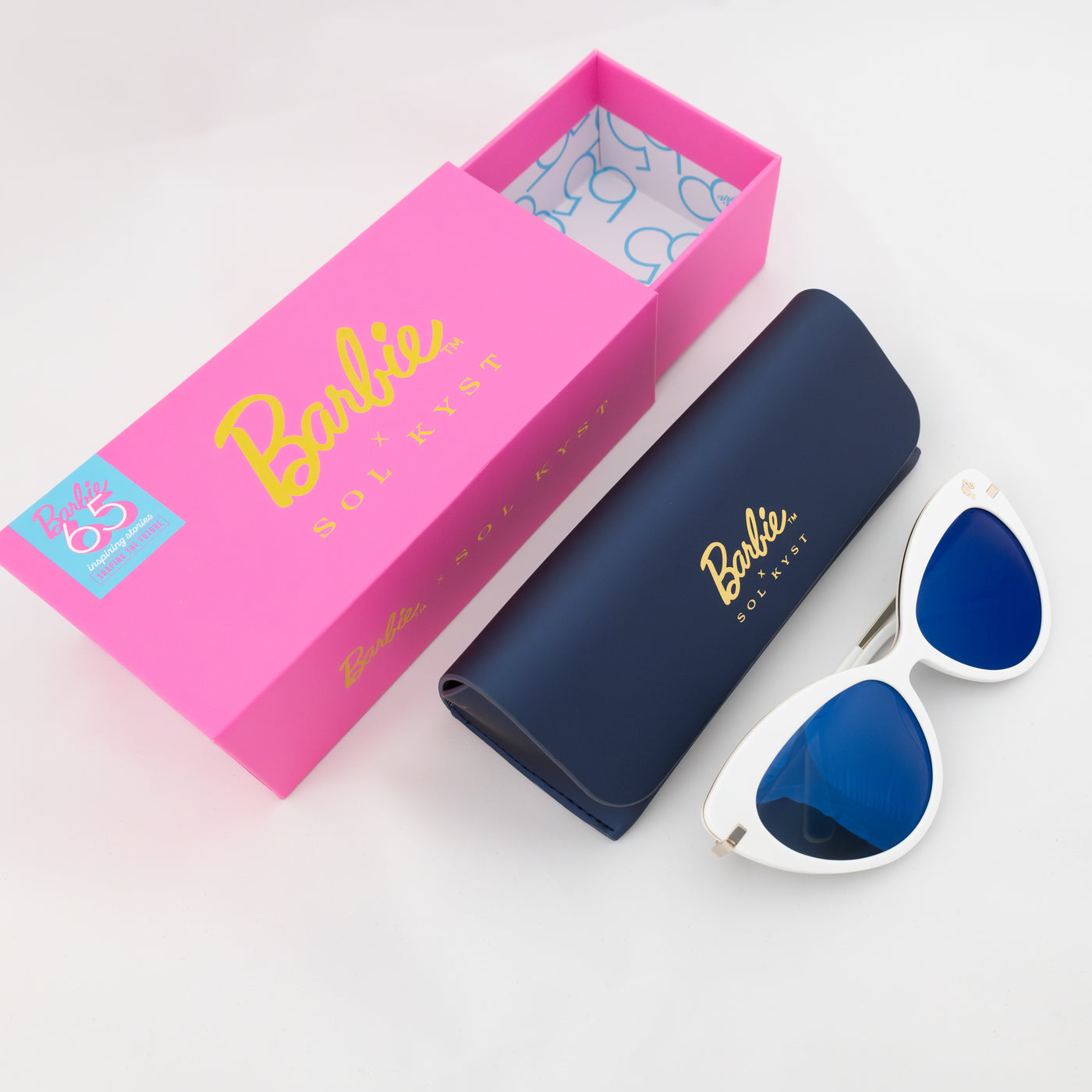 White Barbie cat-eye sunglasses with blue lenses, navy case, and pink 'Barbie x Sol Kyst' box.