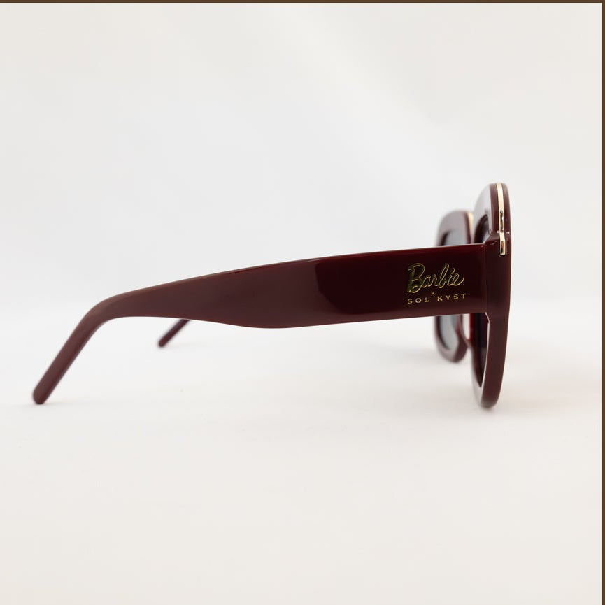Four angles of Barbie Sol Kyst square sunglasses in burgundy with gold reflective lenses, displayed against a white background.