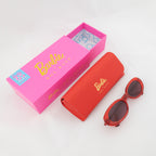 Barbie x Sol Kyst red oval sunglasses with matching red case and vibrant pink packaging.