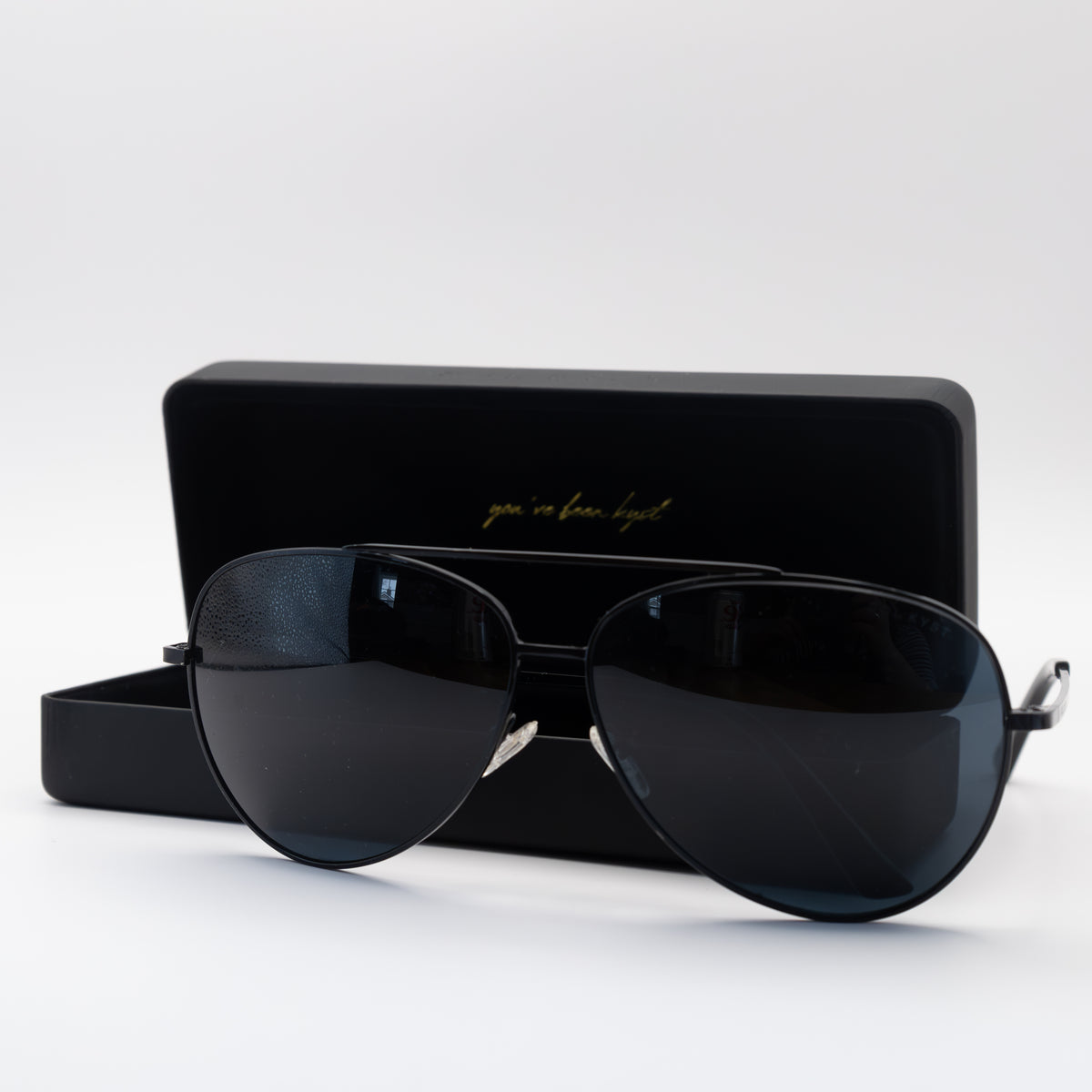 Sol Kyst women's aviators with black frames and dark tinted lenses in front of matching case with a white background.