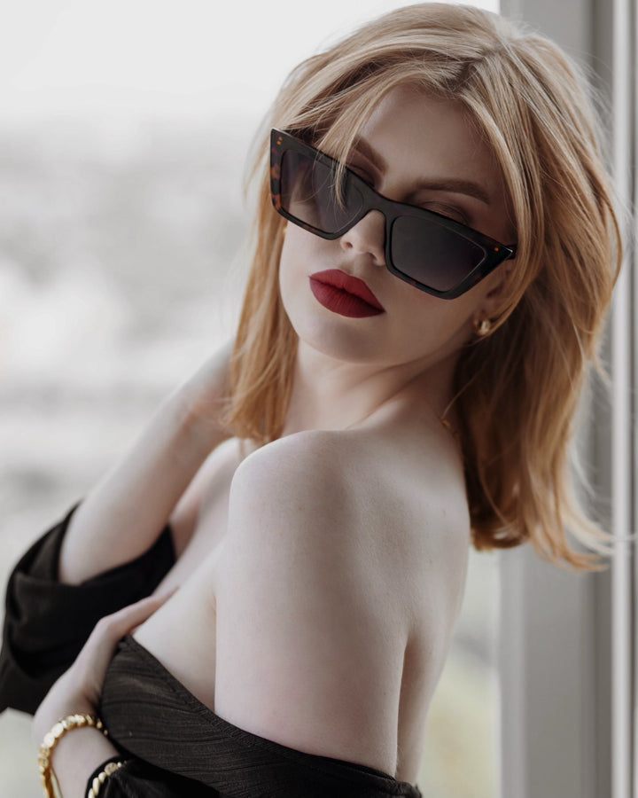 Women in a black dress wearing Sol Kyst trapezoid sunglasses with tortoise frame and gradient lenses.