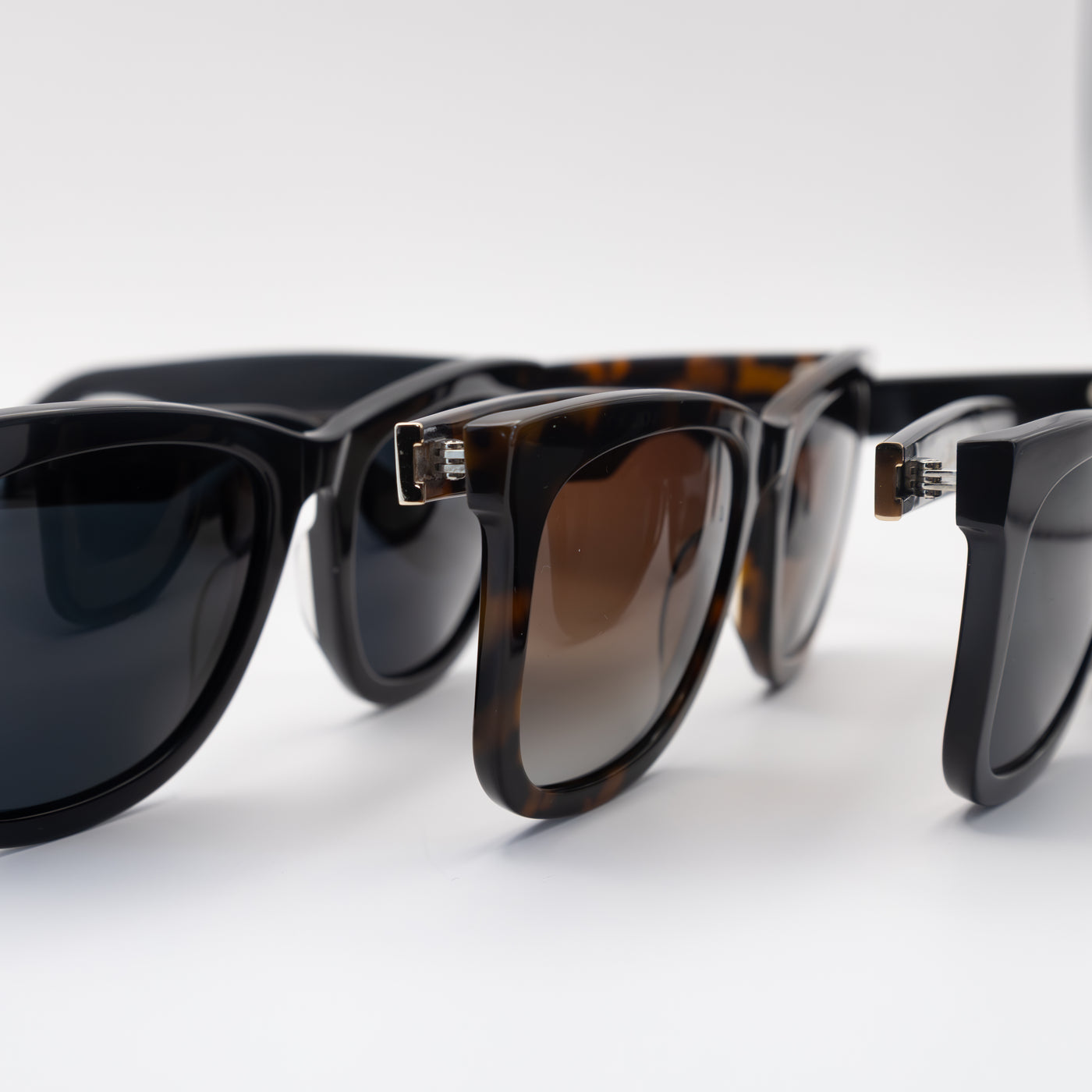 Close-up view of three sunglasses, featuring glossy black and tortoise-shell frames with gradient lenses in a side-by-side arrangement.