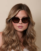 Woman wearing sunglasses with wavy hair against a beige background