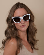 Woman wearing white cat-eye sunglasses against a beige background