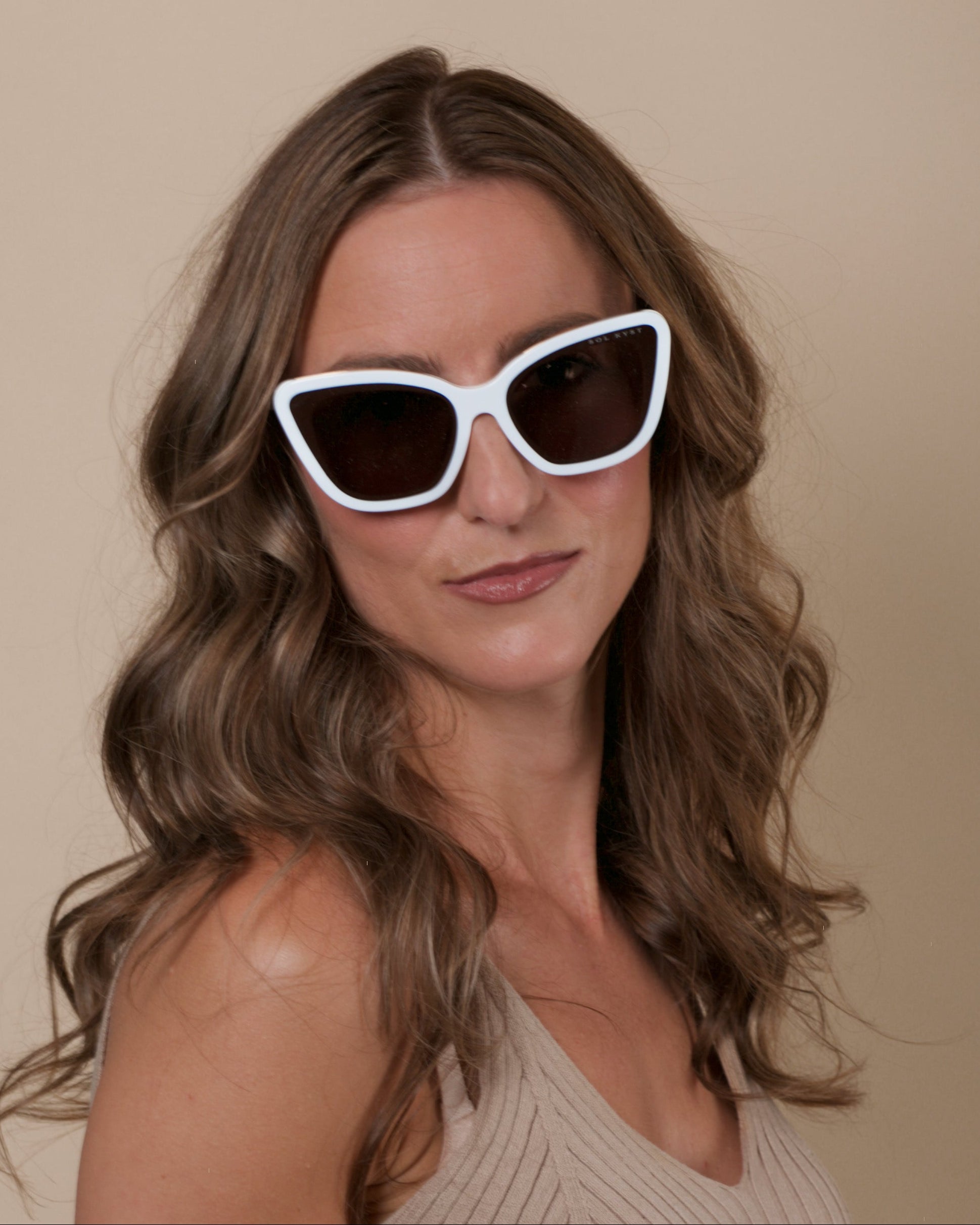 Woman wearing white cat-eye sunglasses against a beige background
