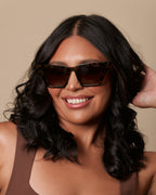 Woman wearing sunglasses and a brown tank top against a beige background
