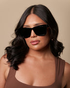 Woman wearing sunglasses and a brown top against a beige background