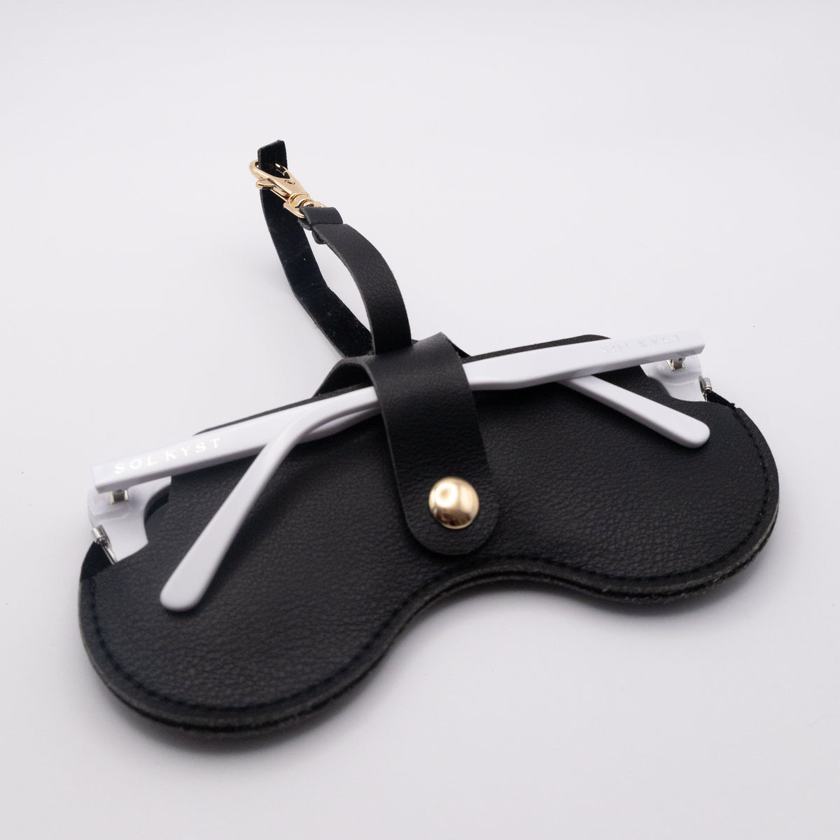 Back view of black Sol Kyst "Kyst Klip" holding sunglasses with white frames on a white background.