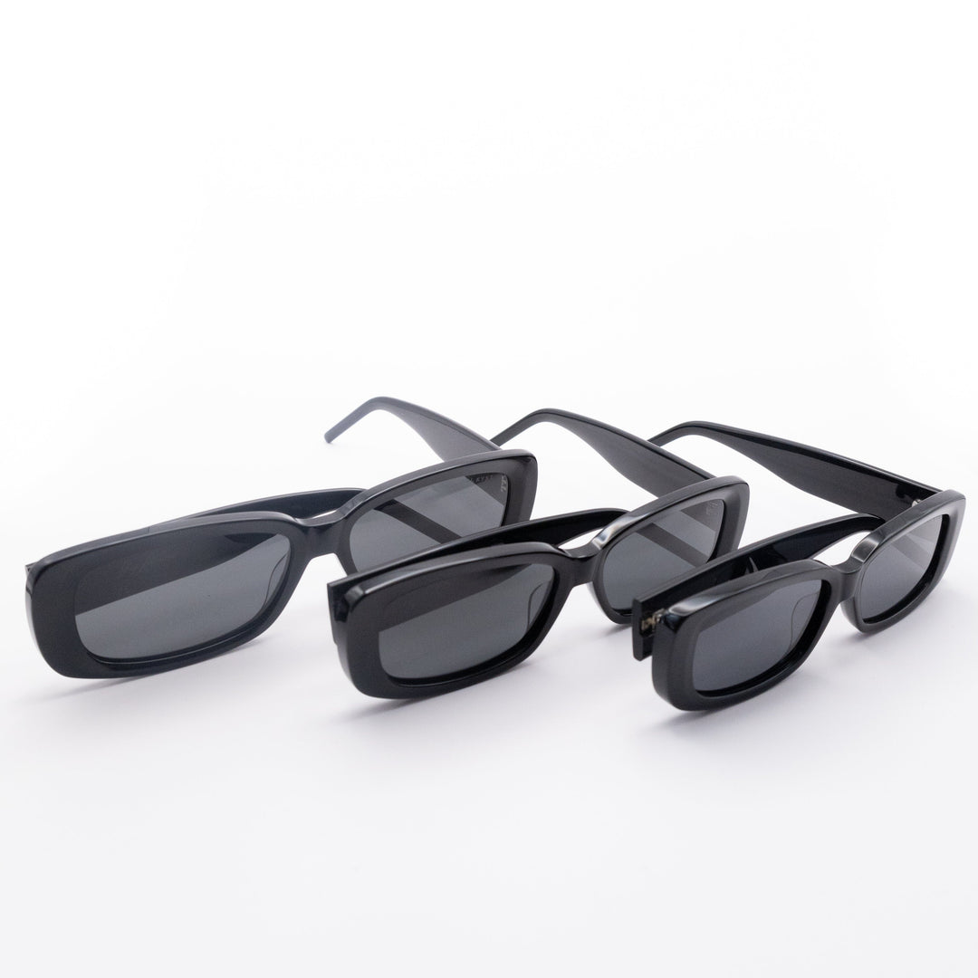 Three Sol Kyst women's rectangle sunglasses with black frames and dark tinted lenses in various sizes in a row.