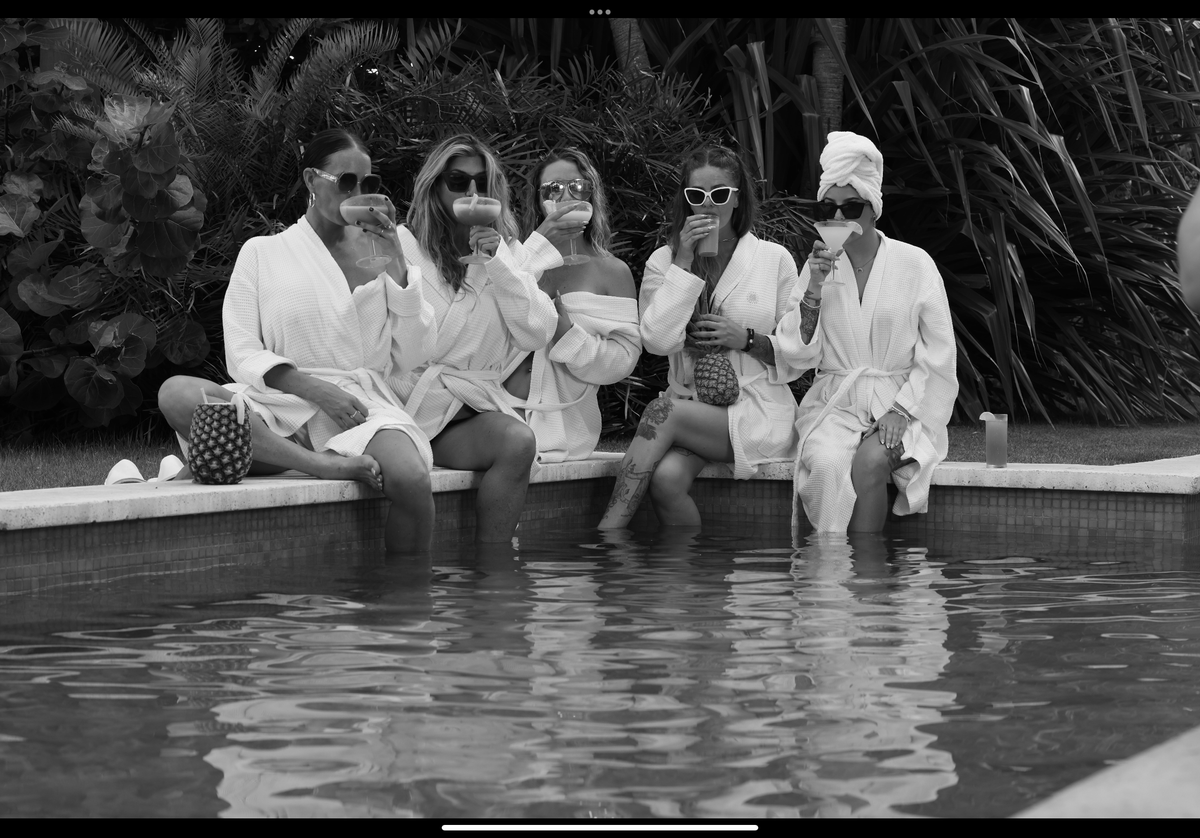 Friends in white robes wearing sunglasses by a pool
