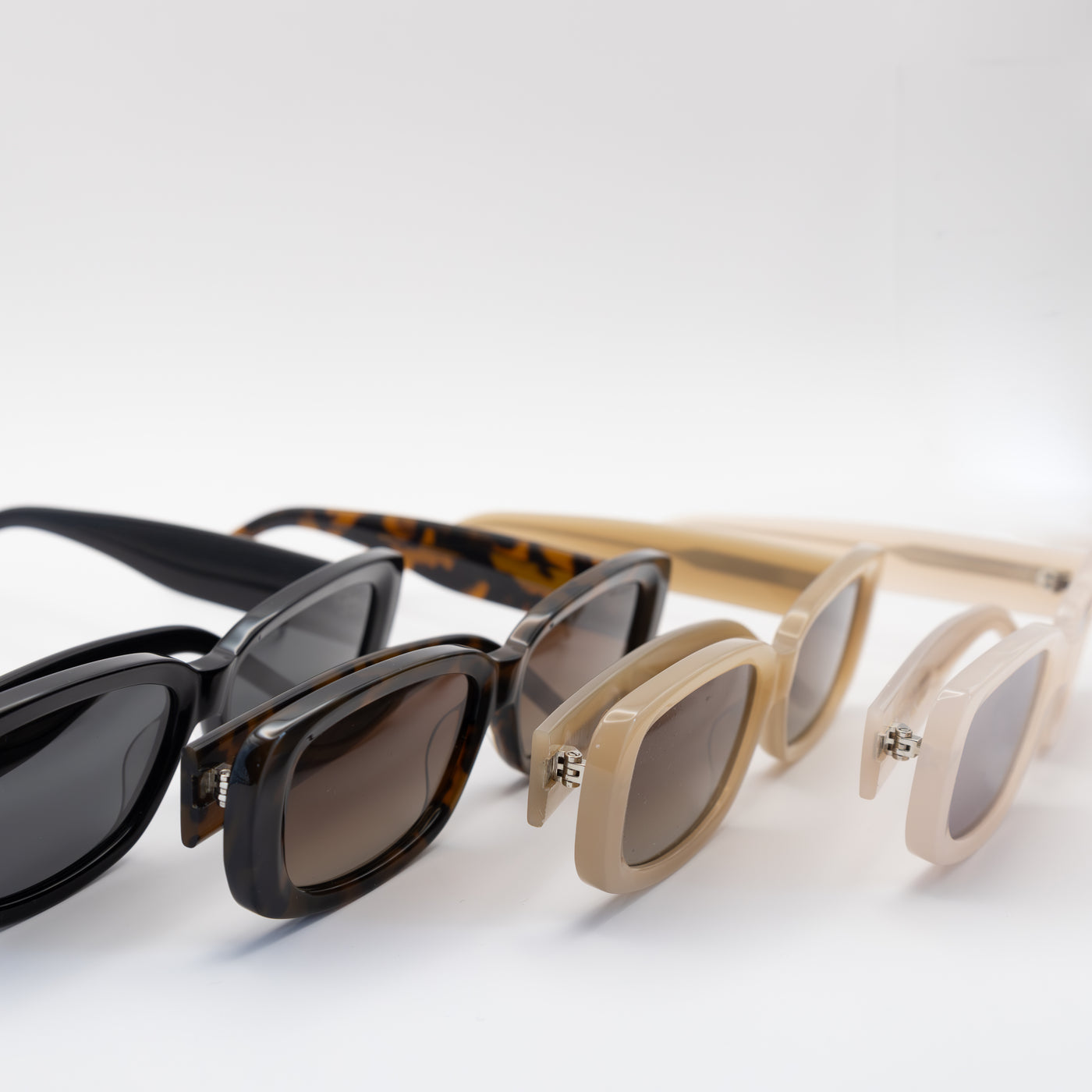 Close-up of beige, tortoise, and black rectangular sunglasses with polarized lenses, showcasing their side profiles.