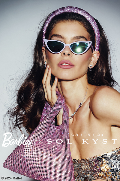 Model wearing lavender Barbie cat eye sunglasses with glossy lenses, paired with a sparkling pink headband and bag.