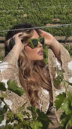 Photoshoot of women in a garden posing with Sol Kyst trapezoid sunglasses with green frames.