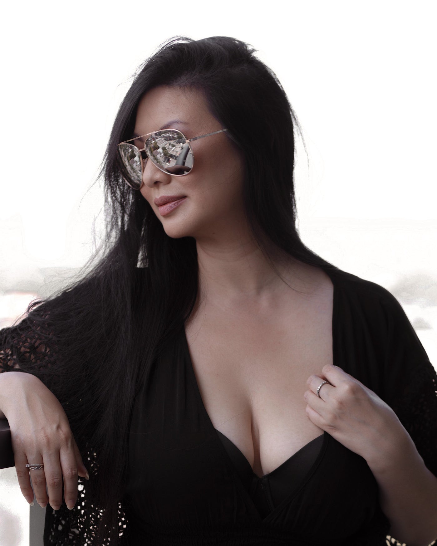 sunglasses, aviator silhouette, wide face sunglasses, rose gold metal frame, mirrored lens, brown ear piece - shown as worn by a women in black, with long dark hair, she is looking off to the side with her arm resting on a balcony railing