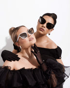 Two models in black strapless dresses, wearing Sol Kyst cat eye sunglasses, one white pair and one black pair.