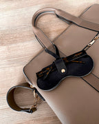Black Sol Kyst "Kyst Klip" holding tortoise sunglasses attached to a tan handbag with a woodgrain background.
